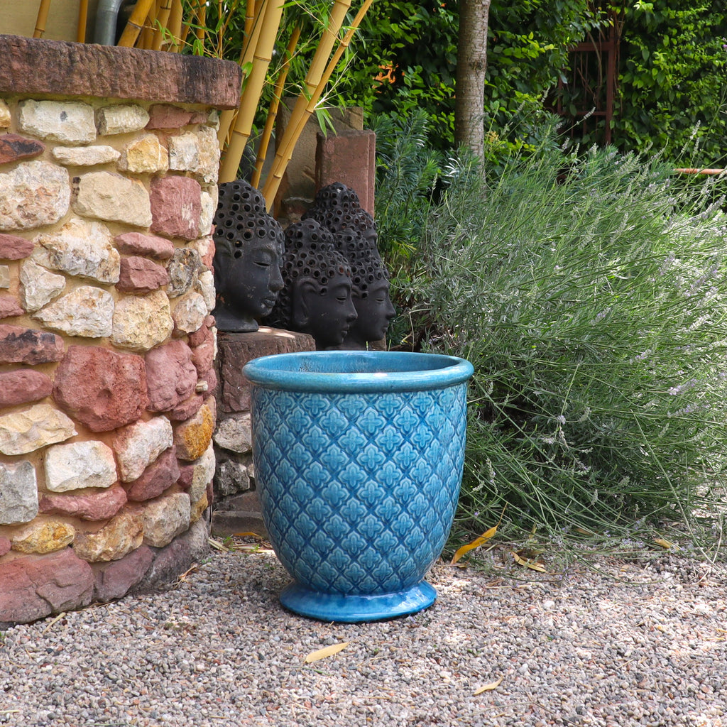 Ein großer Türkis verglaster Blumentopf "Azur Provence" (Höhe 30,5-54 cm) steht auf Kies neben einer Steinmauer. Im Hintergrund sind mehrere schwarze Buddha-Kopf-Skulpturen sowie Bambus, Lavendel und grüne Pflanzen zu sehen.