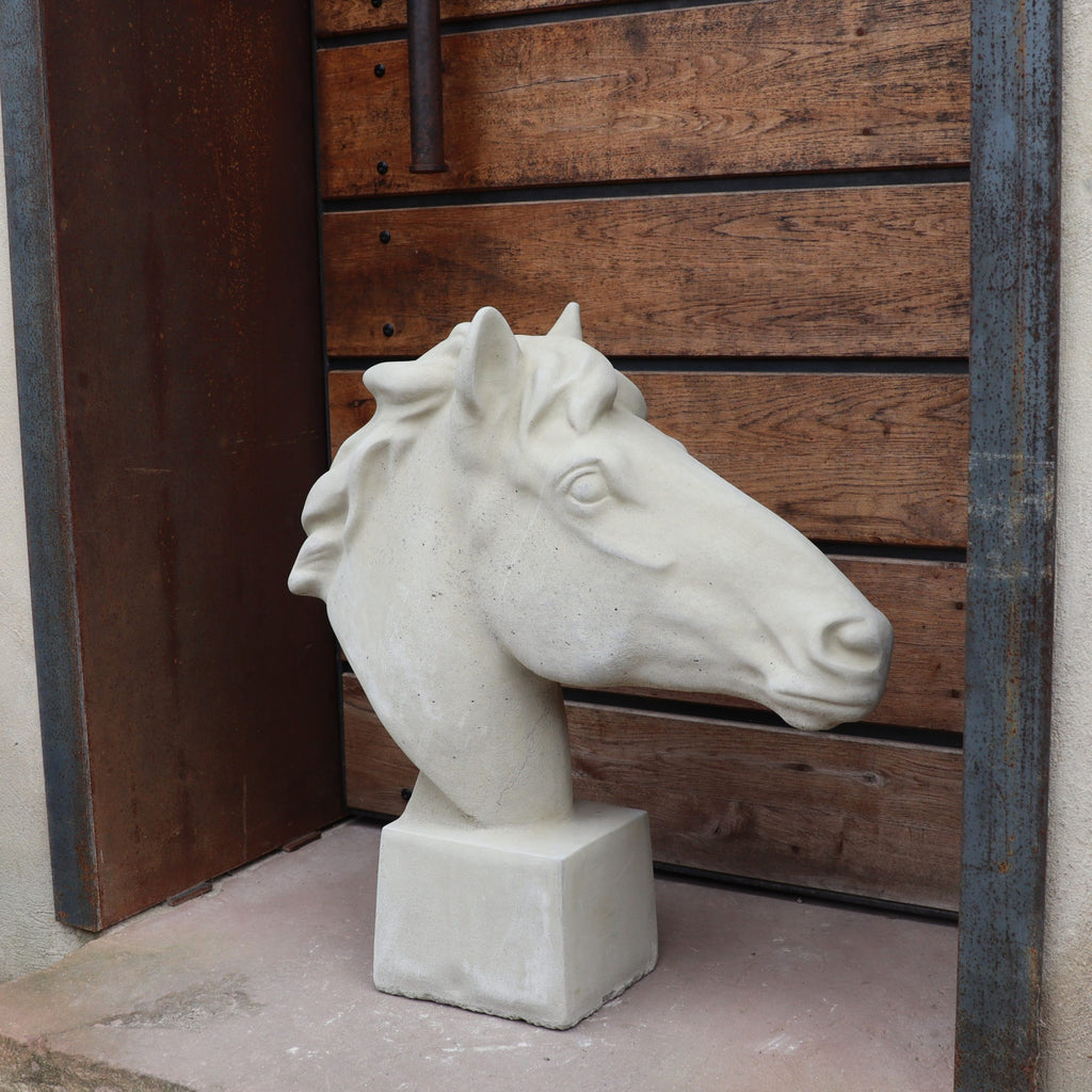 Eine handgefertigte Steinfigur "Pferd groß" in Weiß steht auf einem quadratischen Sockel vor einer Holzverkleidung mit Metallelementen.