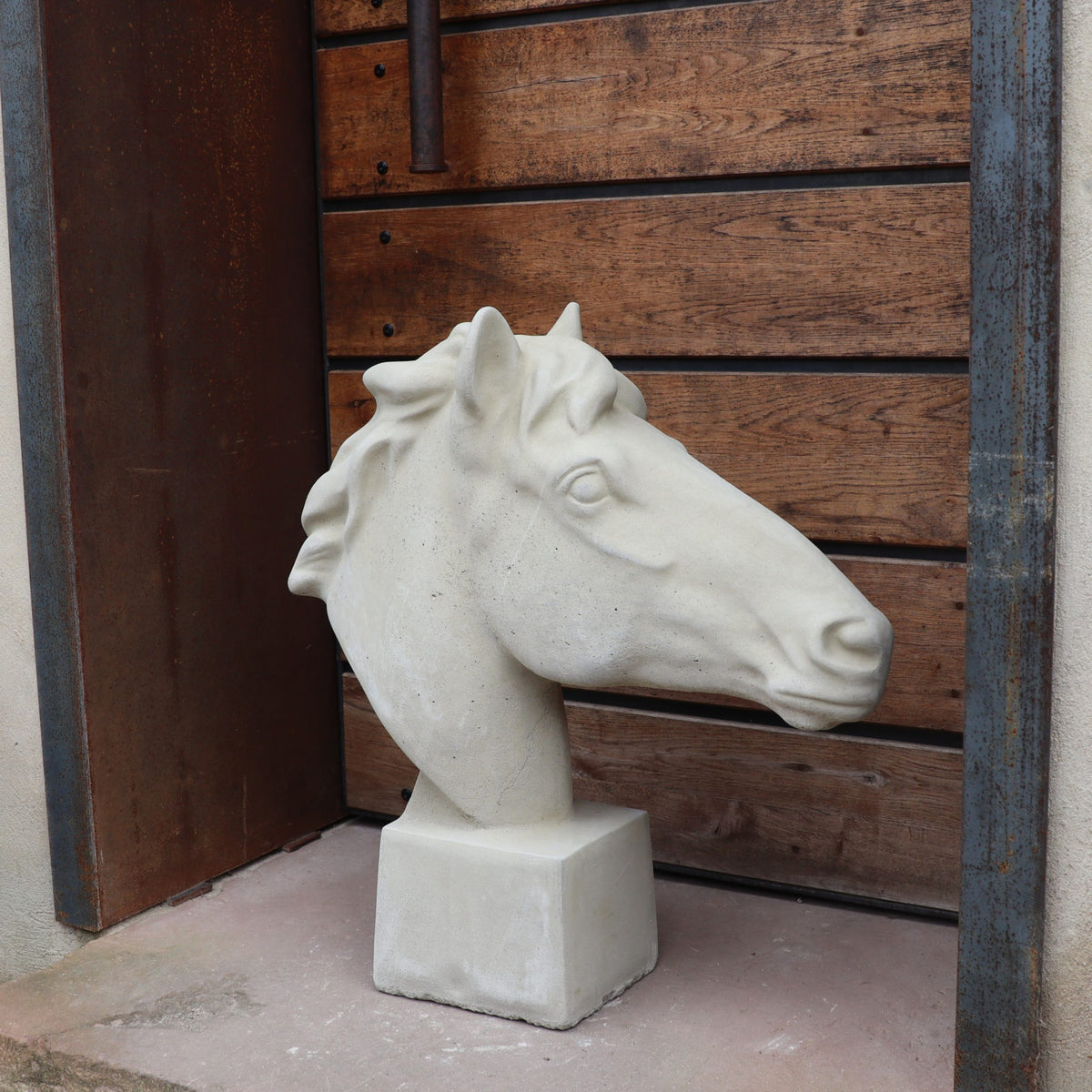 Eine handgefertigte Steinfigur "Pferd groß" in Weiß steht auf einem quadratischen Sockel vor einer Holzverkleidung mit Metallelementen.