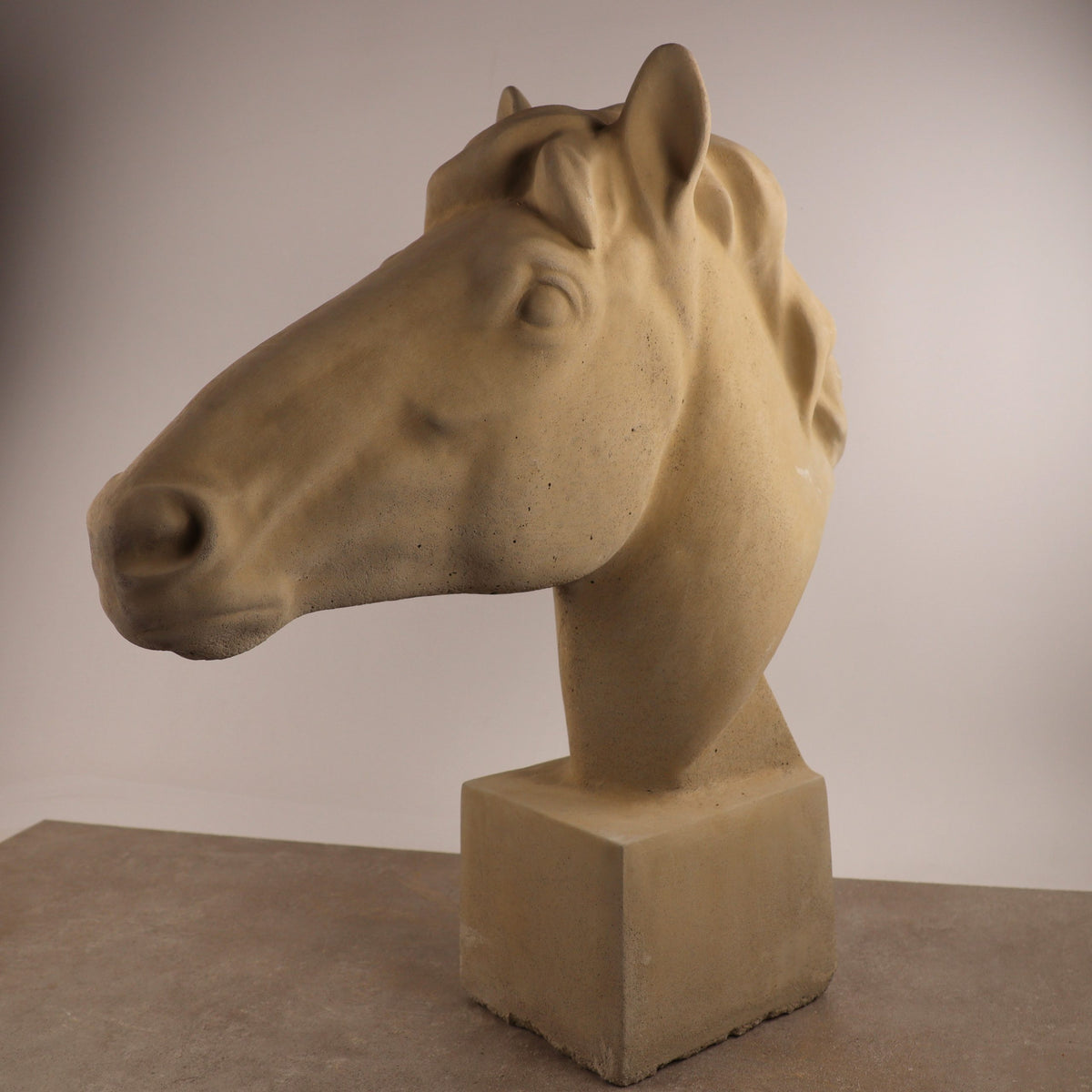 Die handgefertigte Steinfigur "Pferd groß" in Beige steht auf einem quadratischen Sockel. Die realistischen, detailreichen Gesichtszüge machen diese Skulptur vor schlichtem Hintergrund besonders eindrucksvoll.