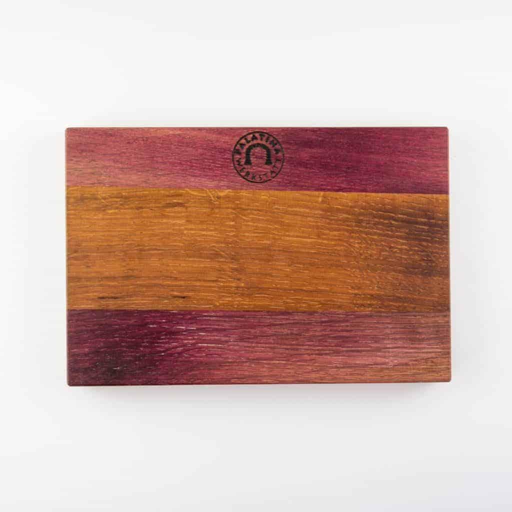 Der Nesmuk Soul Folder, erhältlich mit verschiedenen Griffmaterialien und optionalem handgefertigtem Fassholzbrett, ist ein rechteckiges Holzbrett, das sich durch sein dreifarbiges Design auszeichnet: dunkelrot-violette Streifen oben und unten und ein heller brauner Streifen in der Mitte. Es verfügt über ein geprägtes kreisförmiges Logo in der oberen Mitte des schlichten weißen Hintergrunds.