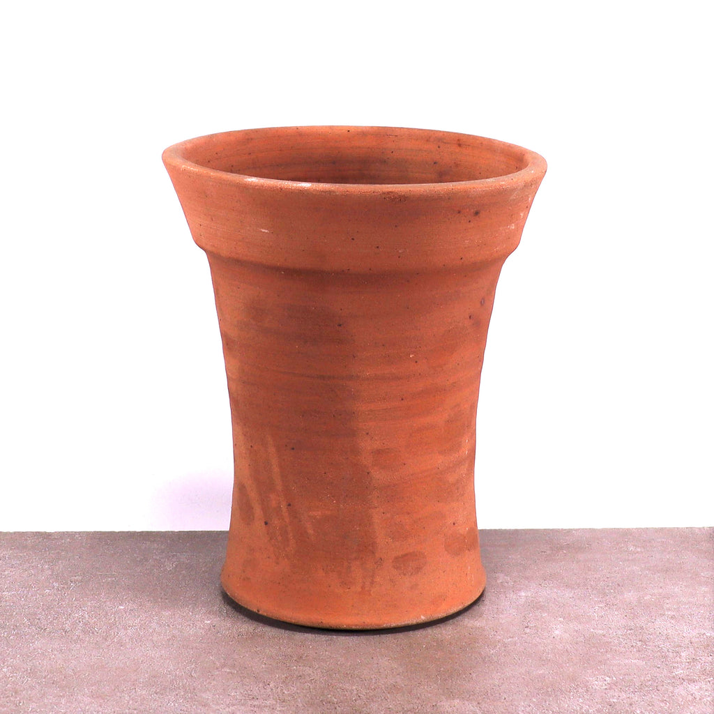 Ein einzelner frostfester Terrakotta-Blumentopf mit leicht ausgestelltem Rand steht auf einer flachen, grauen Oberfläche vor weißem Hintergrund. Der Topf hat eine glatte, aber subtil strukturierte Oberfläche und weist die erdige, rötlich-braune Farbe auf, die für Terrakotta charakteristisch ist.