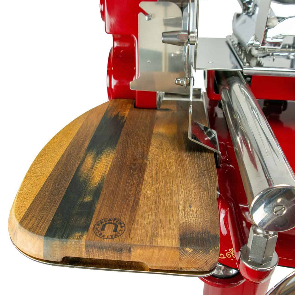 Eine Nahaufnahme der Berkel Volano Tribute Rot, Aufschnittmaschine mit Blumenschwungrad mit Standfuß + Aufschnittbrett aus Fassholz, einer traditionellen Aufschnittmaschine für rotes Fleisch mit einem hölzernen Schneidebrettaufsatz. Das Brett hat abgerundete Ecken und ein markantes Markenlogo. Die Aufschnittmaschine weist metallische Komponenten auf, darunter eine scharfe Klinge und Führungsmechanismen.