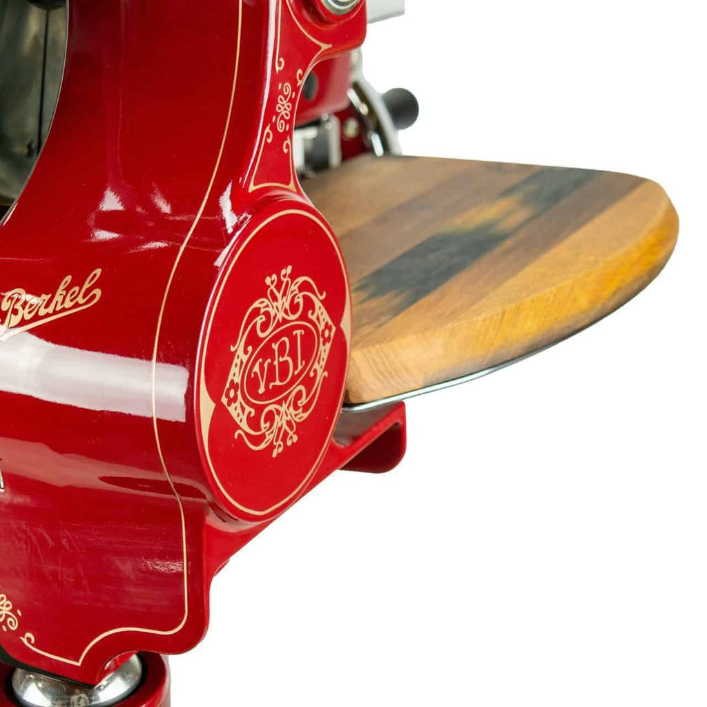 Eine Nahaufnahme des Vintage-Fleischschneiders Berkel Volano Tribute Rot mit floralem Schwungrad und Ständer hebt seine aufwendigen dekorativen Details hervor. Der Schneider ist mit einem Fassholz-Schneidebrett ausgestattet und zeigt sowohl Funktionalität als auch klassische Eleganz.