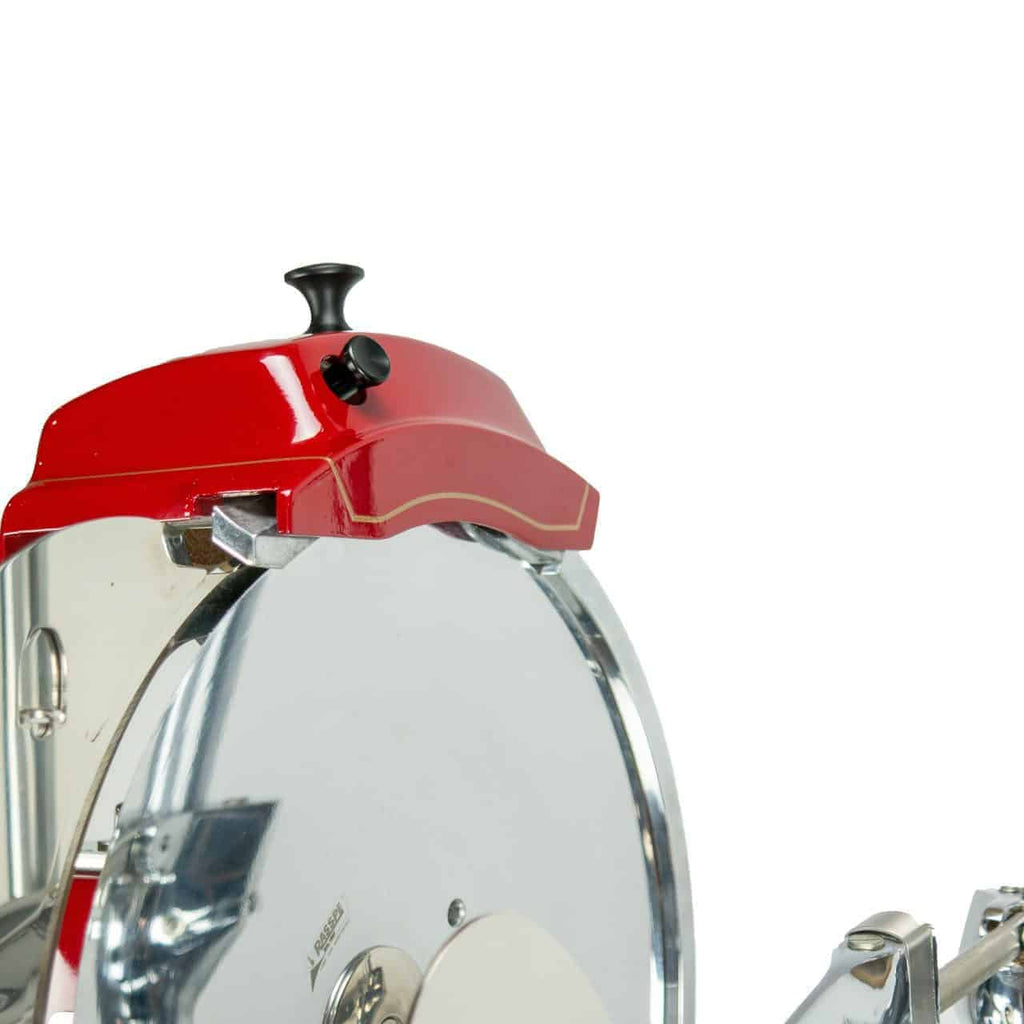 Nahaufnahme der Berkel Volano Tribute Rot, einer Aufschnittmaschine mit Blumenschwungrad, mit großem Rundmesser, silber-rotem Gehäuse mit roter Abdeckung oben, schwarzem Knopf und verschiedenen Metallteilen. Die Maschine verfügt über einen Ständer und ein Aufschnittbrett aus Fassholz. Der Hintergrund ist schlicht weiß.