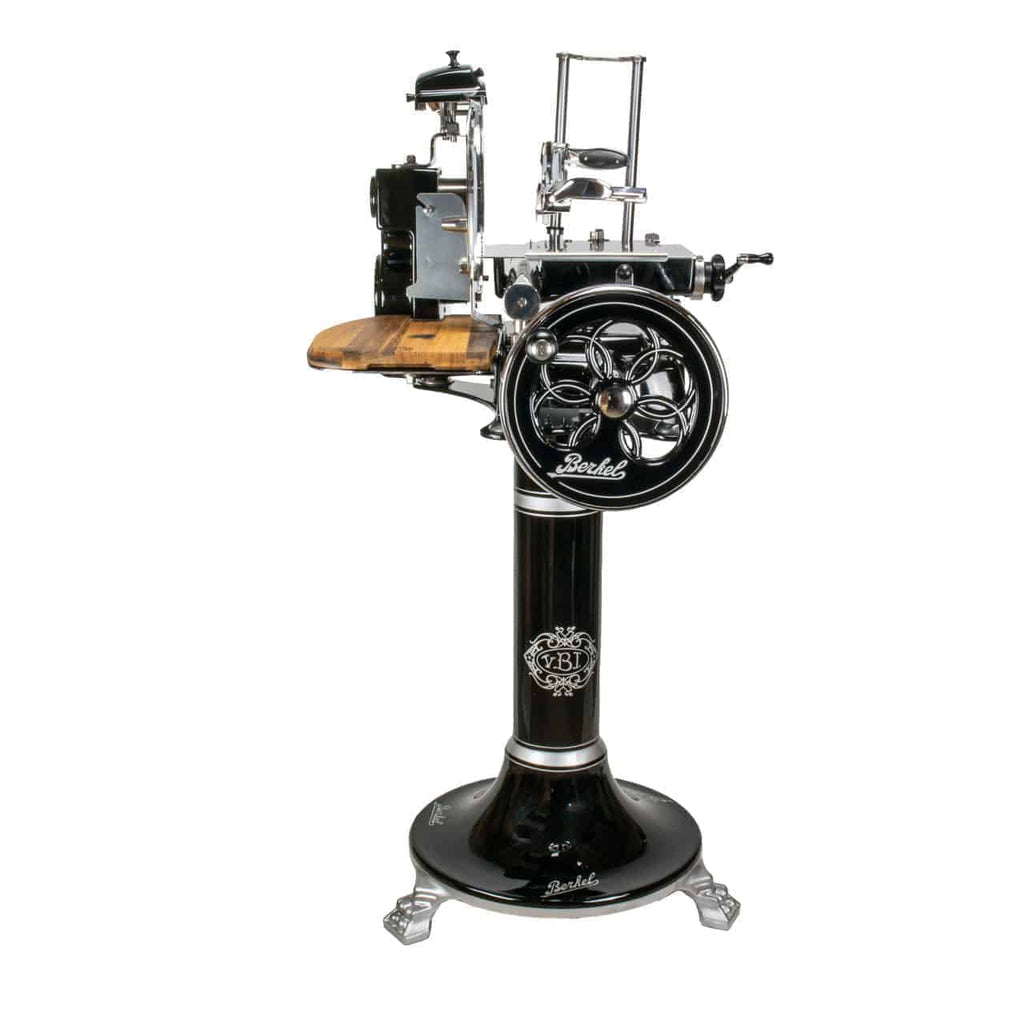 Die Berkel Volano Tribute, eine schwarz-silberne Vintage-Industriemaschine mit aufwendigen Details, trägt die Aufschrift „Berkel“ und steht auf einem hohen Sockel mit einer Oberfläche aus Fassholz. Diese manuelle Aufschnittmaschine enthält verschiedene mechanische Komponenten, Hebel und Zahnräder, was sie ideal für Verarbeitungs- oder Schneidearbeiten macht. Ihr Sockel ist mit kunstvollen floralen Raddesigns geschmückt.