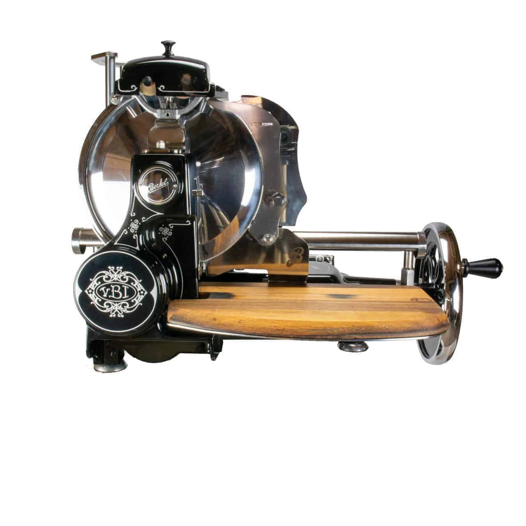 Der Berkel Volano Tribute, ein Vintage-Fleischschneider mit elegantem schwarzen Finish, verziertem Schwungrad mit Blumenmotiv und manueller Bedienung, ist mit einem angebrachten Holzschneidebrett aus Fassholz ausgestattet. Dieser Schneider verfügt über ein großes rundes Messer und polierte Metallkomponenten und ist ein Beispiel für mechanische Präzision und ästhetische Schönheit.