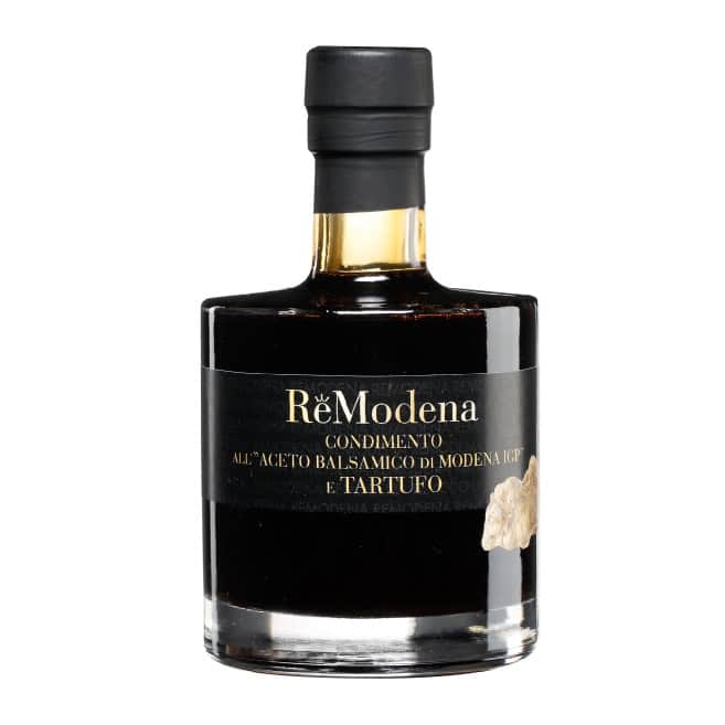 Eine Flasche ReModena Balsamico Essig 250 ml verschiedene Sorten zeichnet sich durch ein schwarzes Etikett mit goldenem und weißem Text aus. Das Design besteht aus einem breiten Boden und einem schmalen Hals mit einer schwarzen Kappe. Das Etikett enthält ein kleines Trüffelbild.