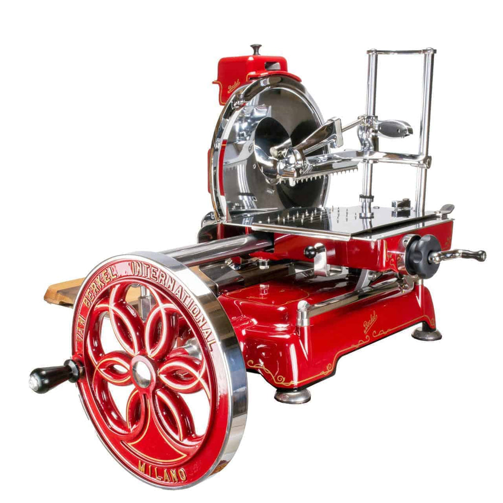 Die Berkel Volano B114 Rot manuelle Aufschnittmaschine mit passgenauem Einlegebrett ist ein Vintage-Aufschnittgerät mit komplizierten Mustern und einem großen runden Messer. Sie verfügt über eine Handkurbel, verzierte Details auf dem Rad und trägt die Aufschrift „Berkel International Milano“. Die Maschine hat eine glänzende, reflektierende Oberfläche und metallische Komponenten.
