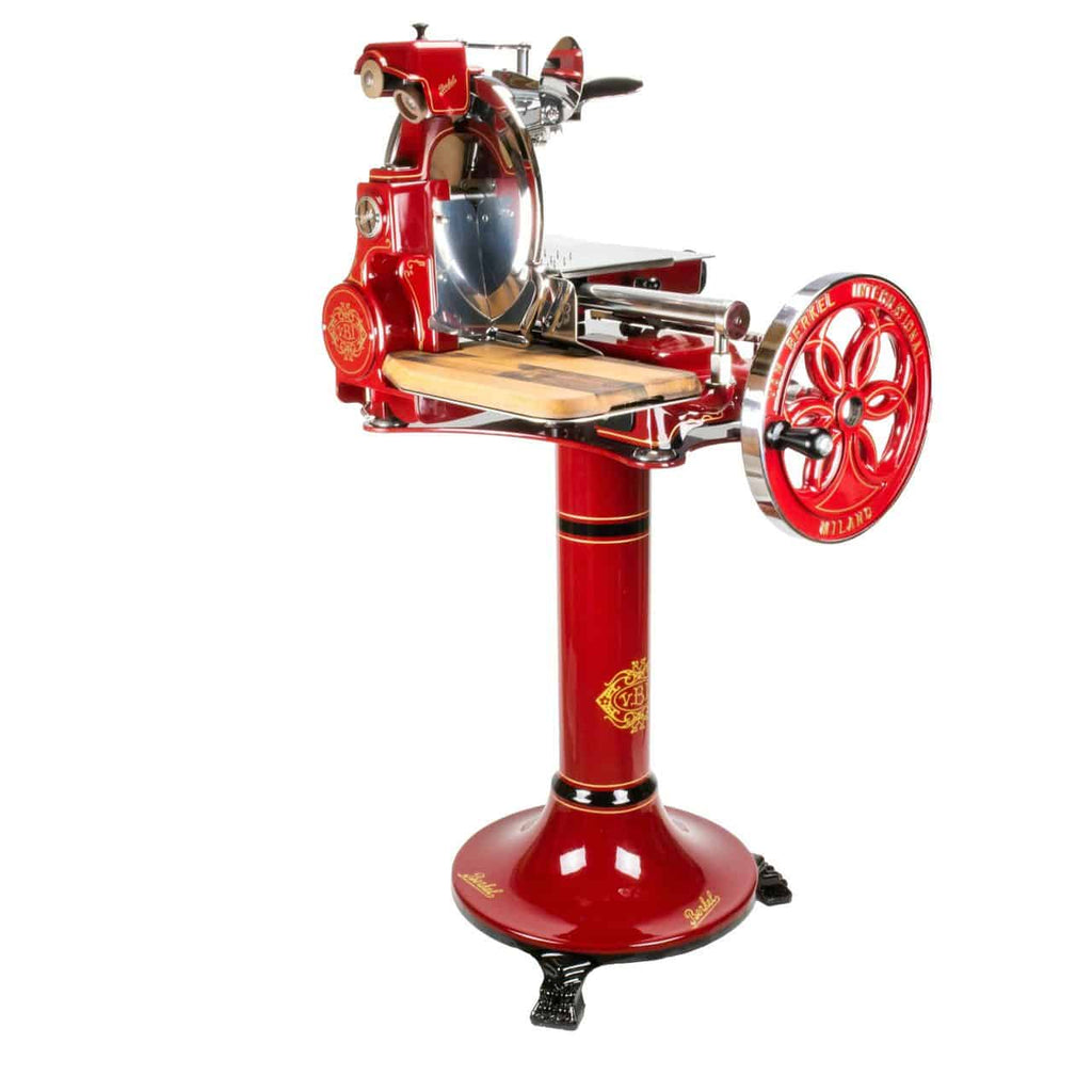 Die manuelle Aufschnittmaschine Berkel Volano B114 Rot mit passgenauem Einlegebrett ist eine rote Aufschnittmaschine im Vintage-Stil, die mit aufwendigen Golddetails verziert und auf einem passenden Standfuß montiert ist. Sie verfügt über ein großes Schwungrad mit Handkurbel an der Seite sowie ein rundes Messer zum Schneiden. Diese manuelle Aufschnittmaschine verfügt außerdem über ein hölzernes Einlegebrett und Metallkomponenten.