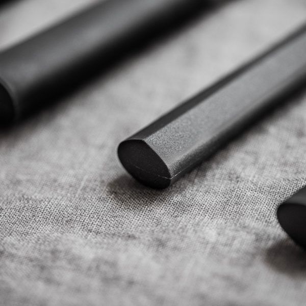 Nahaufnahme der KAI Weihnachtsangebot 4-teiliges Geschenkset - Wasabi Black-Komponenten, bestehend aus schlanken, schwarzen, zylindrischen Objekten mit glatten, abgerundeten Enden. Sie sind auf einer strukturierten grauen Oberfläche platziert und das Bild fängt ihre feinen Details und ihr mattes Finish ein. Als Teil dieses Sets in limitierter Auflage (nur 1.000 Stück verfügbar) sind diese Teile wahrscheinlich ein wesentlicher Bestandteil eines modernen Designprodukts oder -werkzeugs.