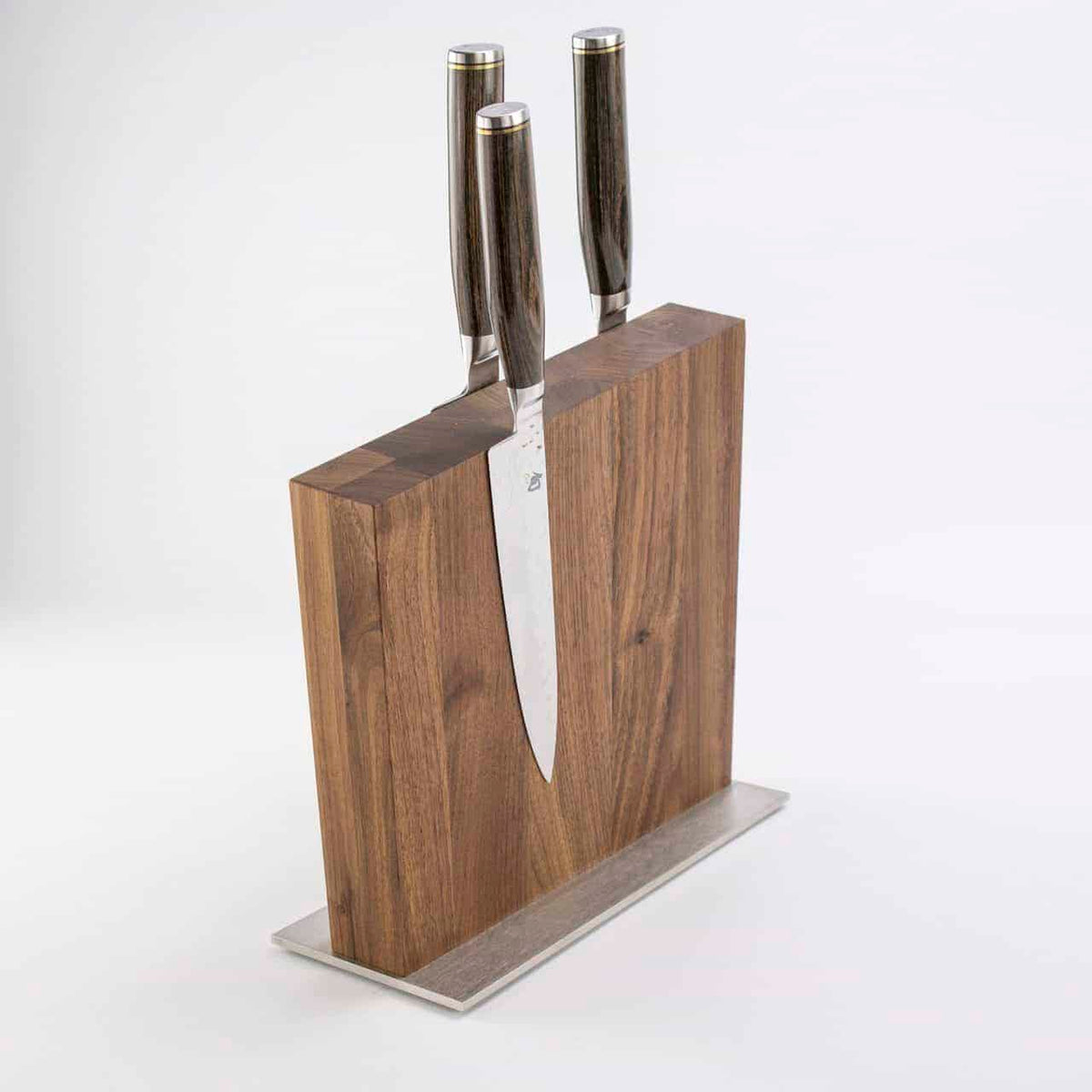 Produktname: „Exklusives Messerblock Set, KAI Shun Tim Mälzer Damastmesser mit hochwertigem Magnet-Messerblock Böker“ Ein exklusives Messerblock Set mit einem luxuriösen magnetischen Holzmesserblock von Böker, der drei elegante KAI Shun Tim Mälzer Damastmesser mit dunklen Griffen enthält, ist montiert ein schlanker rechteckiger Metallsockel. Die Messer sind gleichmäßig verteilt und teilweise in den hochwertigen Magnet-Messerblock Böker eingesetzt, wobei ihre glänzenden Klingen stolz zur Schau gestellt werde