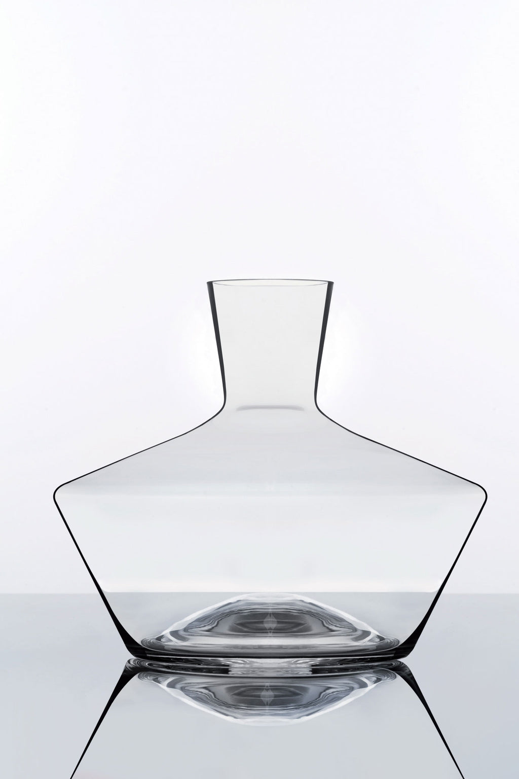 Eine minimalistische Karaffe aus klarem Glas mit breitem Boden und schmalem Hals steht vor einem schlichten weißen Hintergrund. Die Reflexionen der darunterliegenden verspiegelten Oberfläche erzeugen einen symmetrischen Effekt und betonen die klaren Linien der Karaffe.